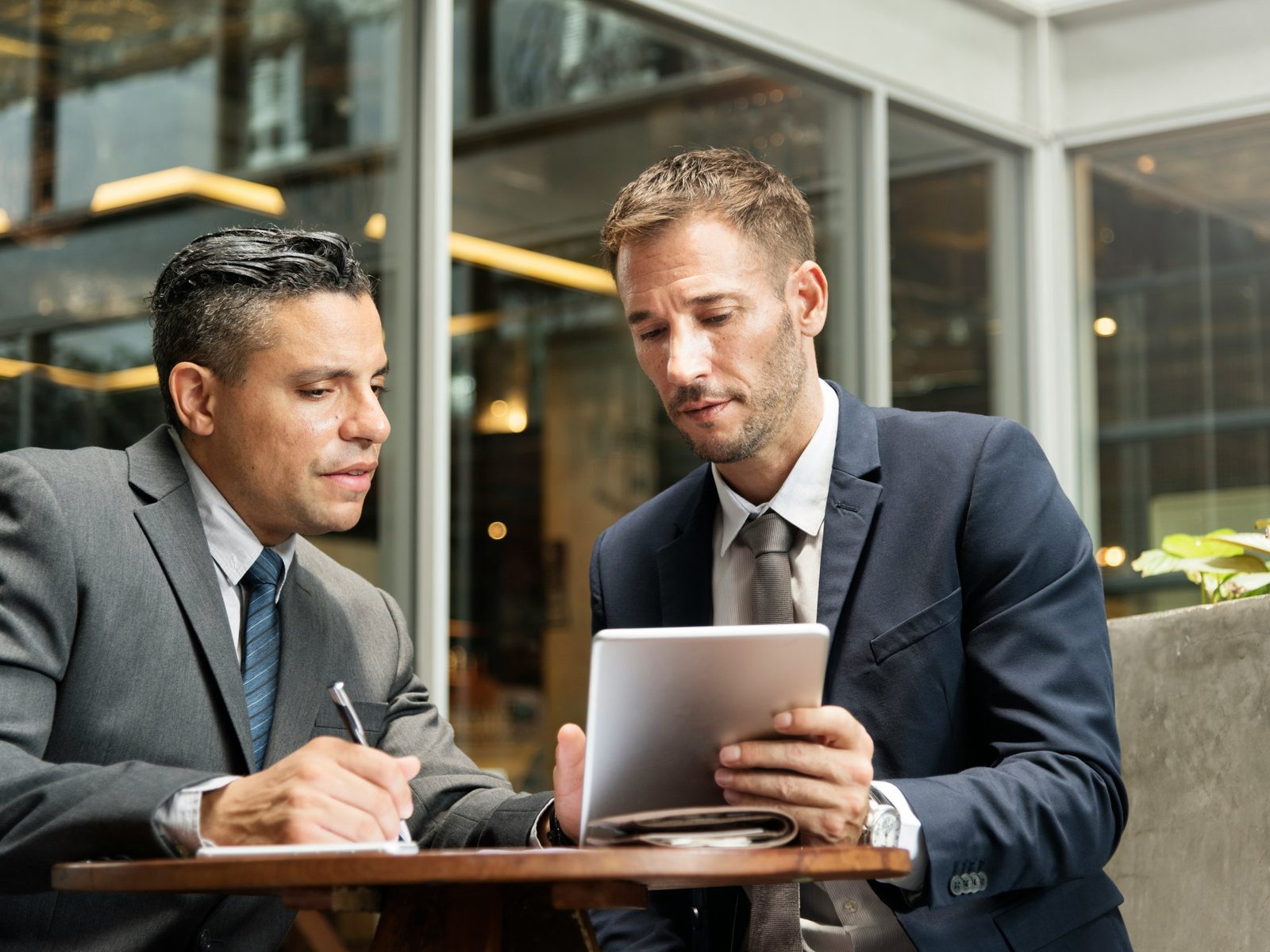 Two businessmen reviewing notes and a tablet at a cafe table