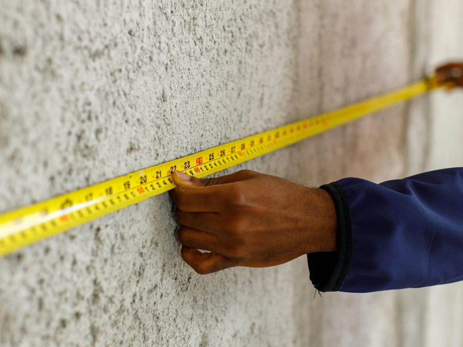 A hand holding a yellow tape measure against a concrete wall