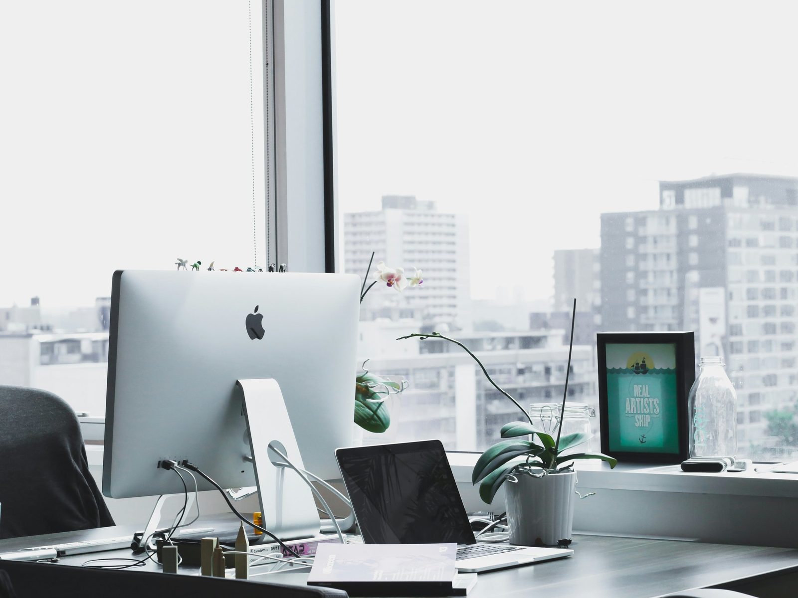 An empty desk with a computer by a window overlooking a city