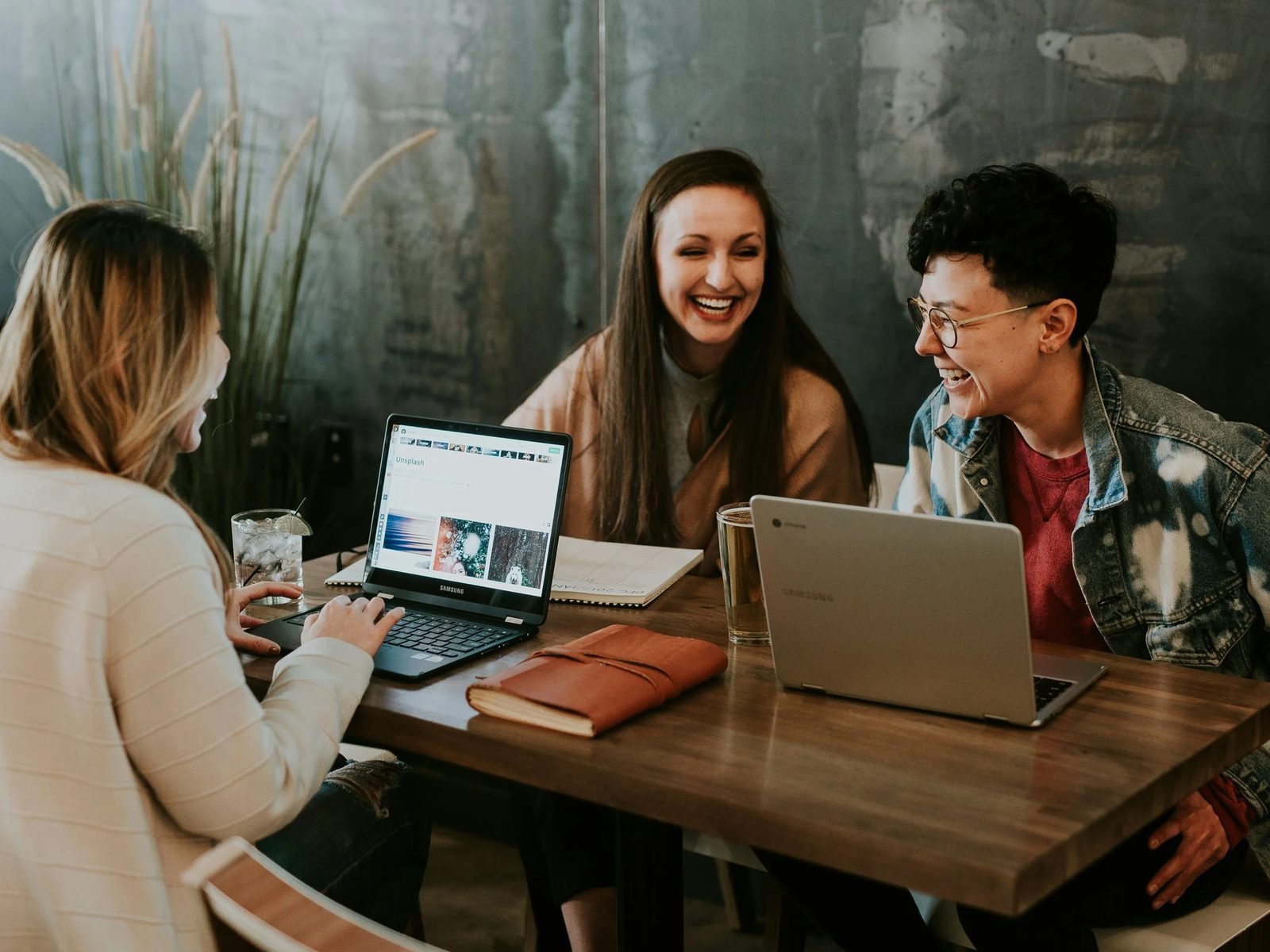 Three colleagues laughing together at a table with laptops