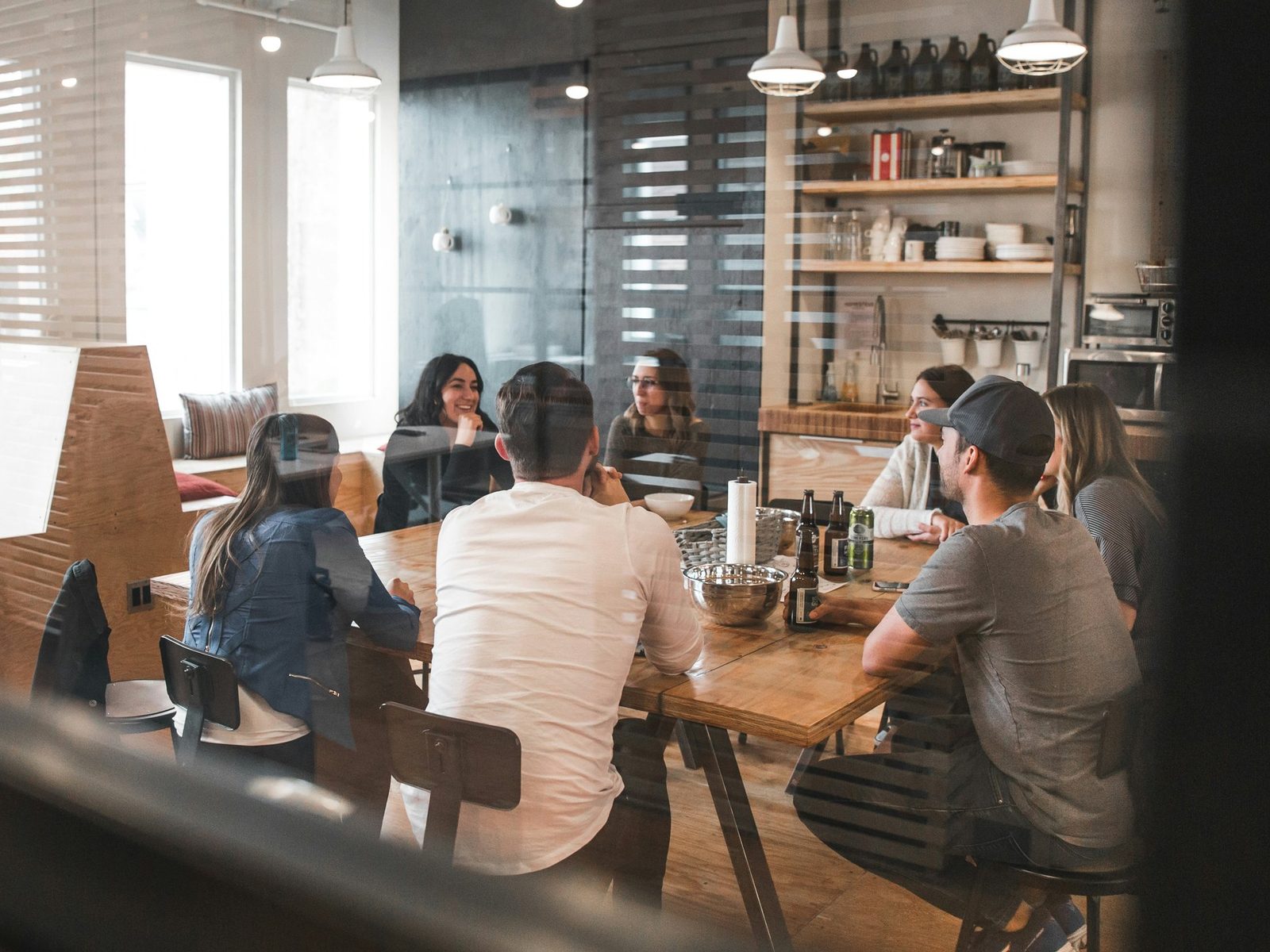 A team meeting at a long wooden table, seen through a window