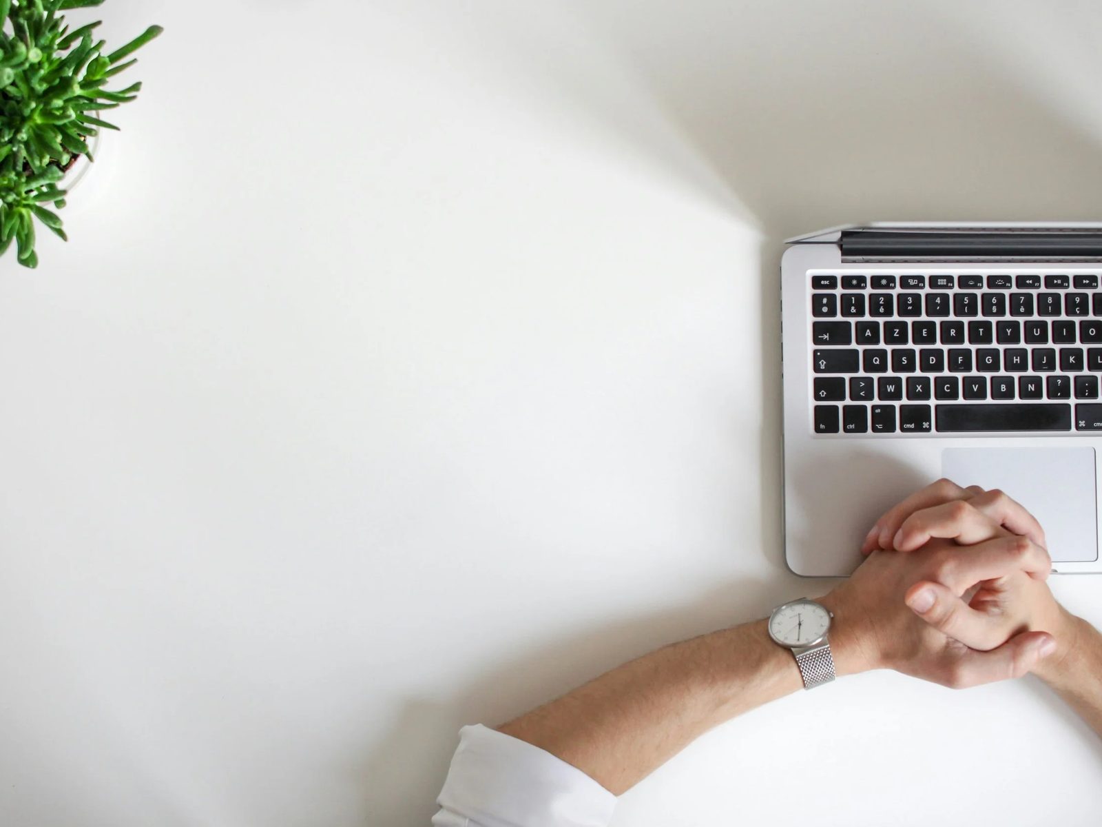 Clasped hands resting beside a laptop on a white desk