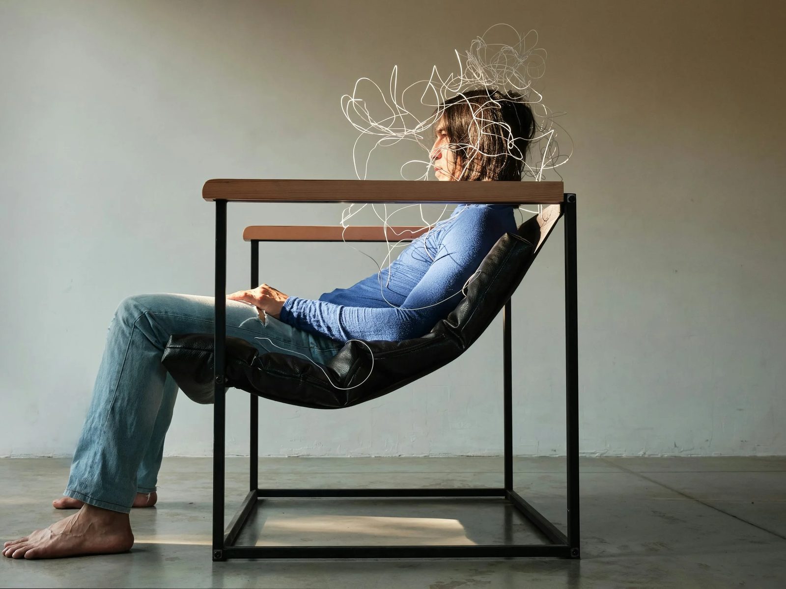 A person reclining in a steel frame chair with a tangle of white wire around their head